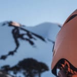Un esquiador con casco naranja en la cima de una montaña nevada disfrutando de la experiencia Andesgear.