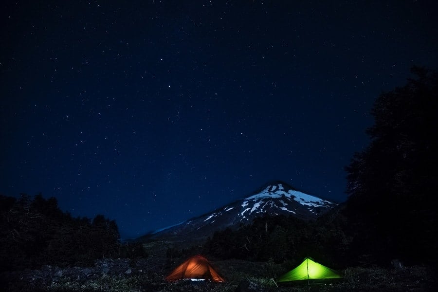 Dos tiendas de campaña bajo un cielo estrellado con una montaña en la noche.