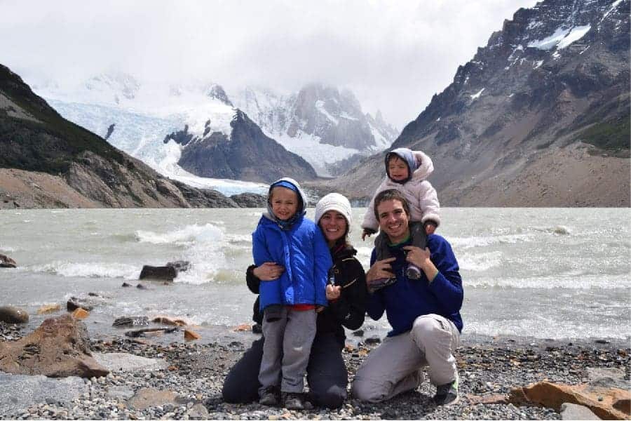 Una madre y su familia posando para una foto cerca de un lago con montañas al fondo.