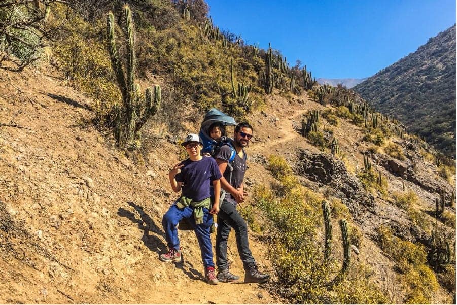 Dos personas caminando por un sendero con cactus al fondo en el terreno accidentado.