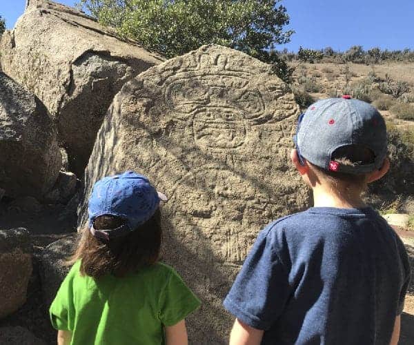 Dos niños de la región norte observan una gran roca con un grabado.