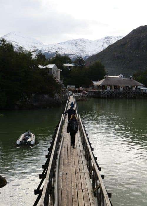 Un puente de madera sobre un lago con montañas de tortel al fondo.