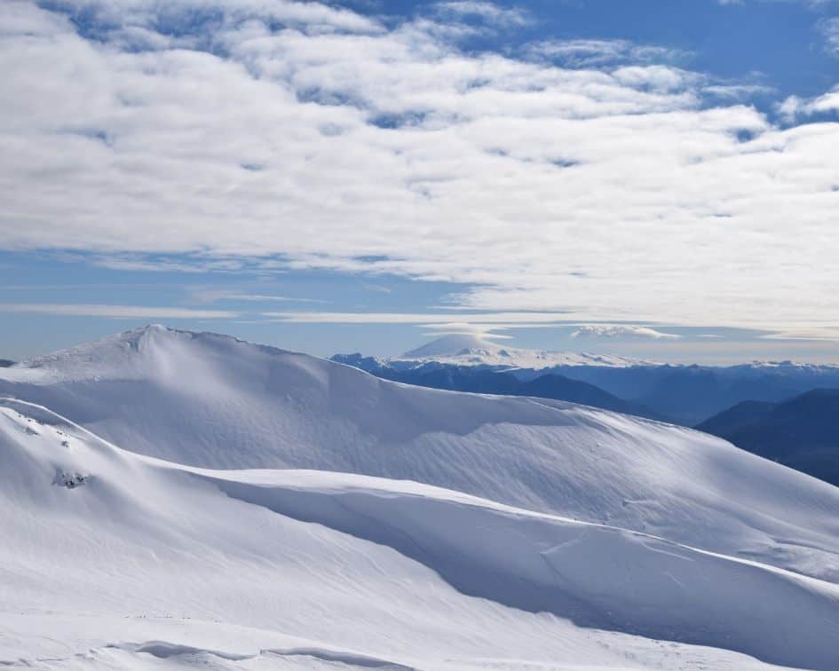 Una persona está parada en la cima de una montaña cubierta de nieve, disfrutando del entorno sereno e impresionante.