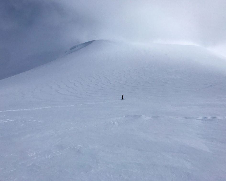 Una persona está parada en la cima de una montaña cubierta de nieve, contemplando el impresionante entorno.