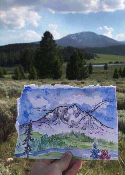 Vicki Speck sosteniendo una pintura en acuarela de una montaña.