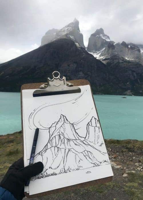 Un arte que muestra la mano de Vicki Speck sosteniendo un portapapeles con un dibujo de una montaña.