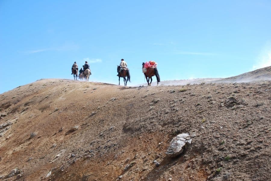 Una cabalgata de gente montando a caballo por una colina.