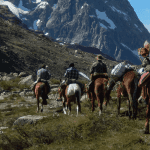 Un grupo de personas participando en una cabalgata en una zona montañosa.
