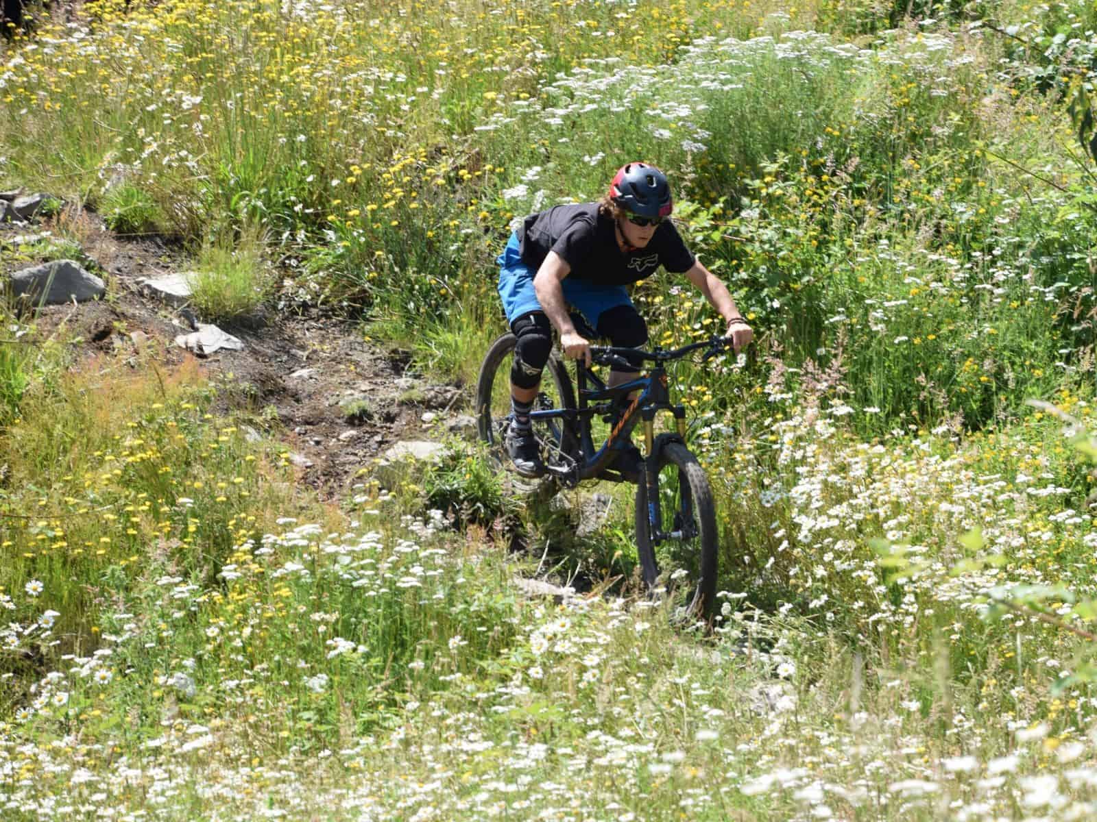 Un hombre en una bicicleta de montaña huilo huilo acelerando a través de un campo de flores silvestres.
