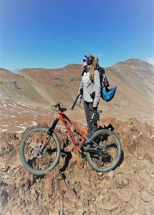 Una mujer parada en la cima de una montaña con su gran bicicleta de montaña.