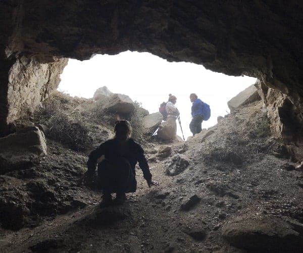 Un grupo de personas paradas en la entrada central de una cueva.
