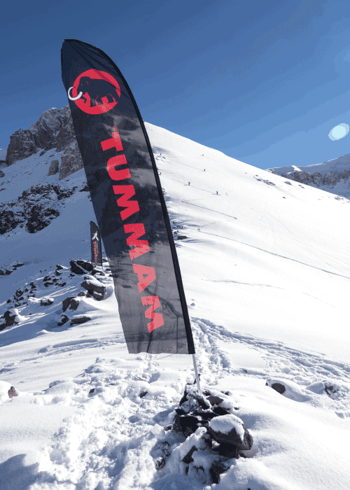 Una bandera alpina con la palabra tumma está en la cima de una montaña nevada.
