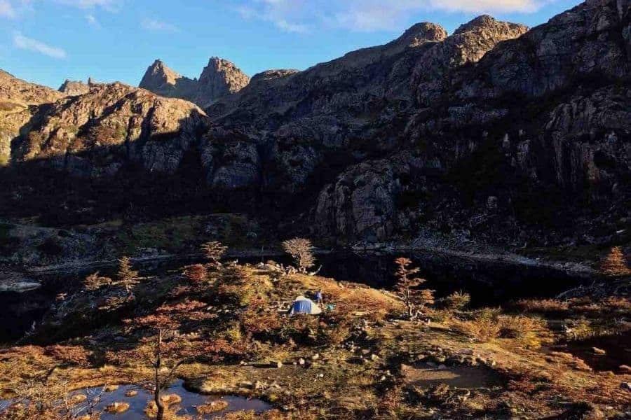 Una persona acampando en la cima de una montaña con un lago al fondo.