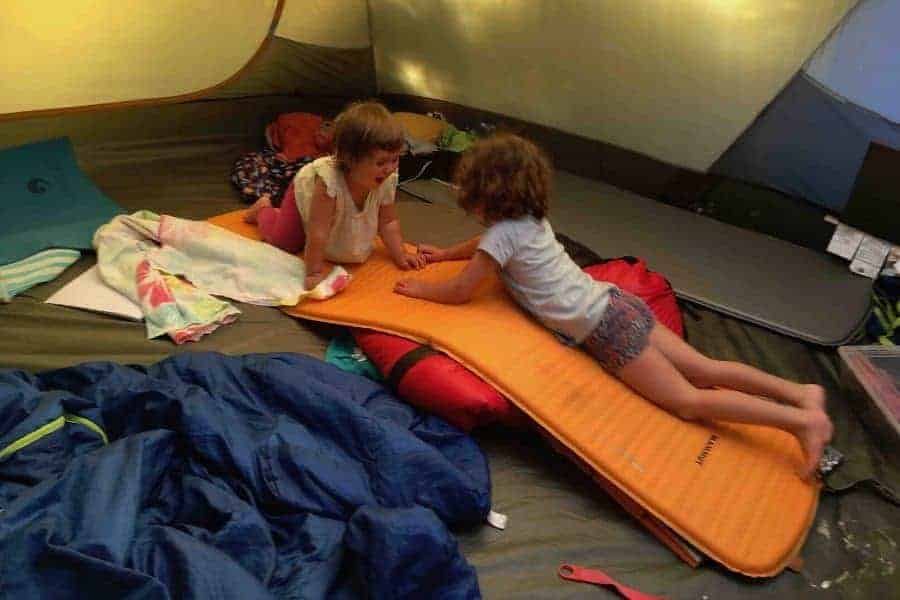 Dos niños sentados en una colchoneta en una tienda de campaña.