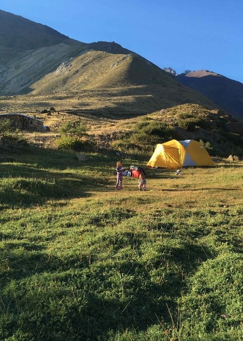 Dos niños acampando en un campo de hierba con montañas al fondo.