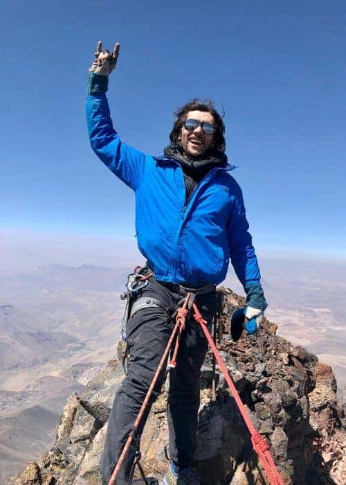 Un hombre con una chaqueta azul parado en la cima del Cerro Campanario, una montaña majestuosa.