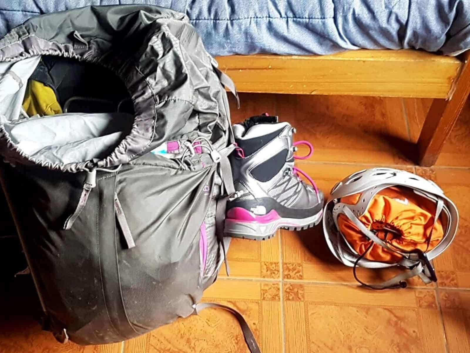 Una mochila de montañismo está sentada sobre un suelo de baldosas junto a un saco de dormir de andinismo.