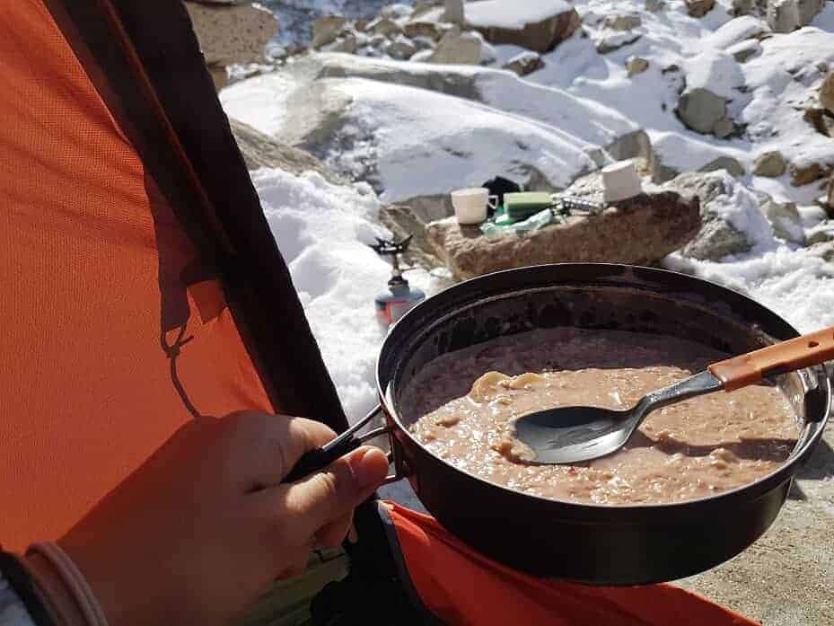 Una persona sosteniendo una olla de sopa en una tienda de campaña en la montaña mientras practica andinismo.