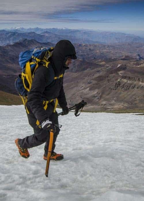 Un hombre practicando montañismo, subiendo una montaña nevada con una mochila en la alta.
