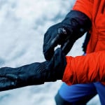 Una persona vestida con una chaqueta roja sosteniendo un par de guantes para montañismo en altura.