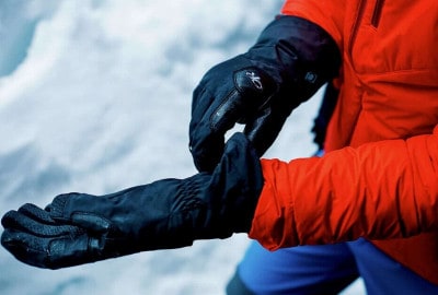 Una persona vestida con una chaqueta roja sosteniendo un par de guantes para montañismo en altura.