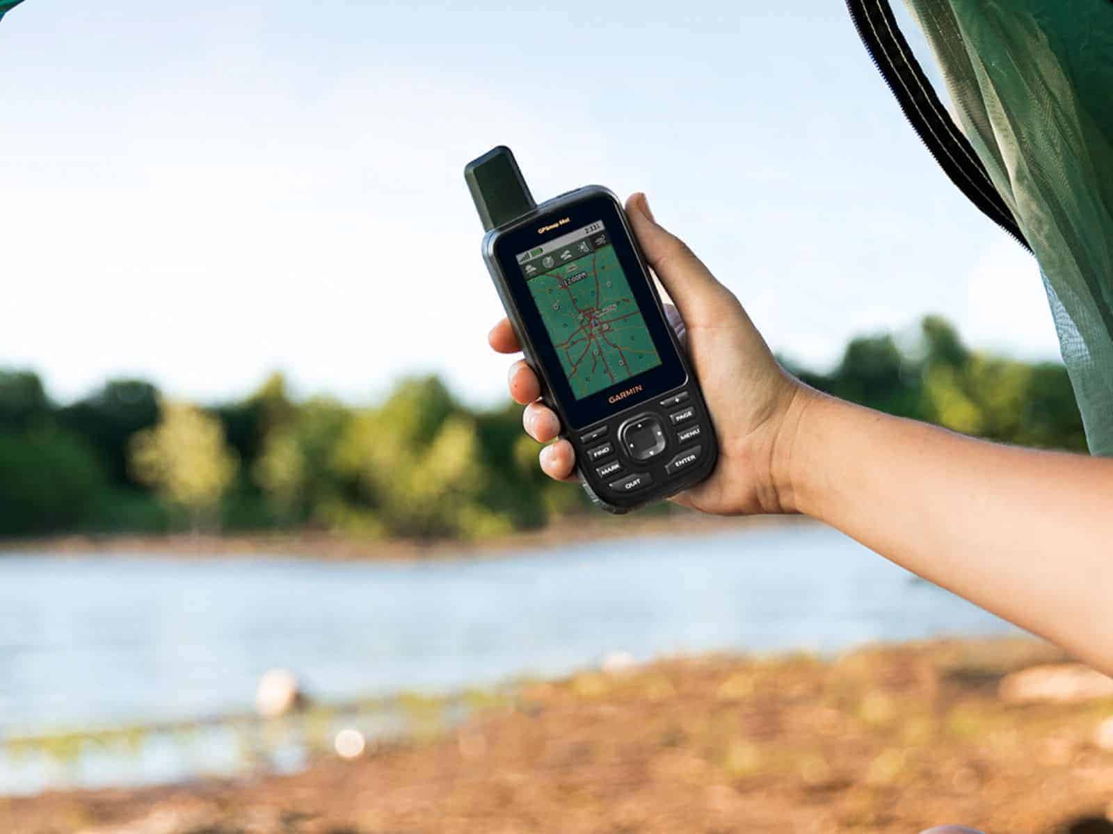 Una persona sosteniendo un dispositivo GPS Garmin junto a un lago sereno.