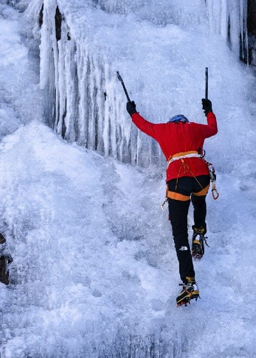 Un hombre con una chaqueta roja y un piolet Anker trepa por una cascada helada.