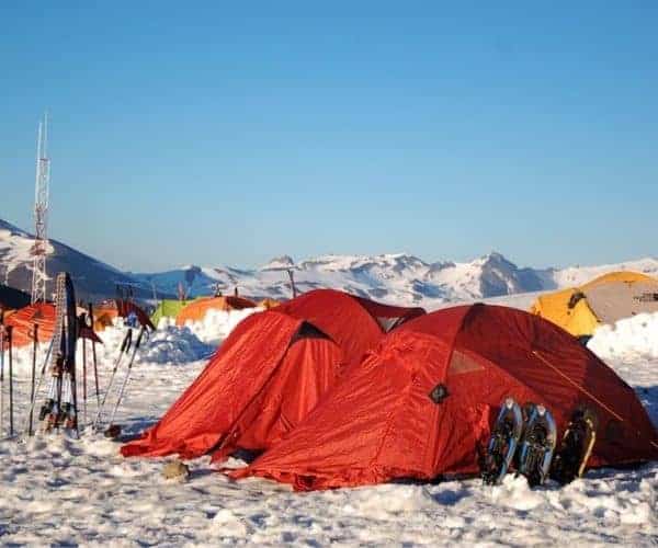 Una carpa en la nieve con esquís al fondo.