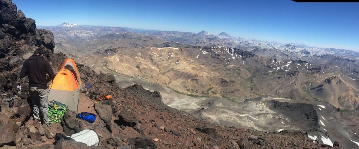 Un hombre está escalando una montaña con una carpa en la cima.