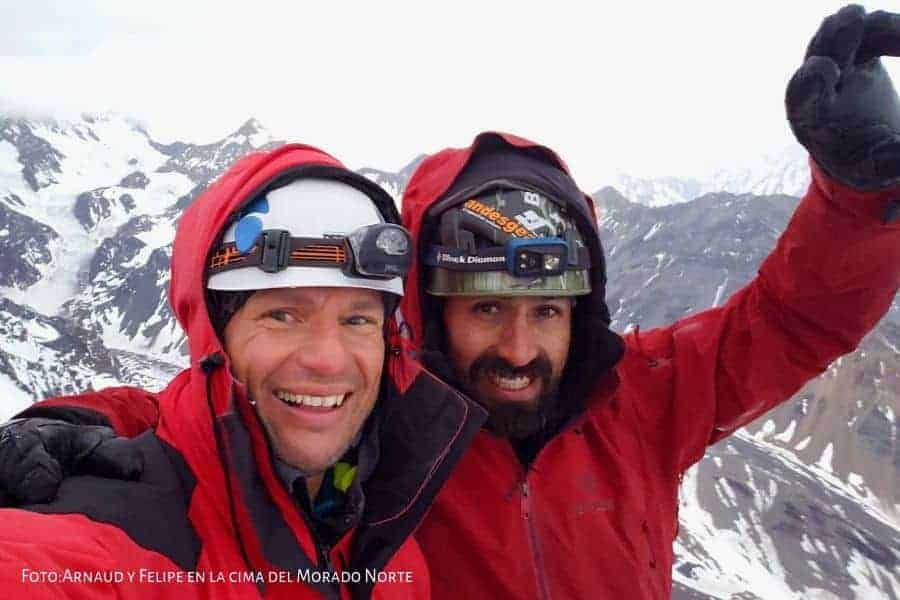 Dos hombres con chaquetas rojas parados en la cima de la montaña El Morado.