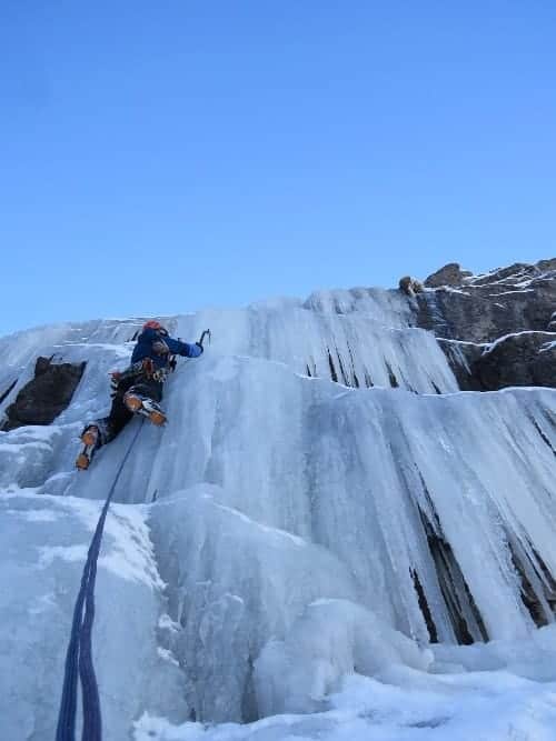 Descripción: Un escalador de hielo sube por un acantilado cubierto de hielo.