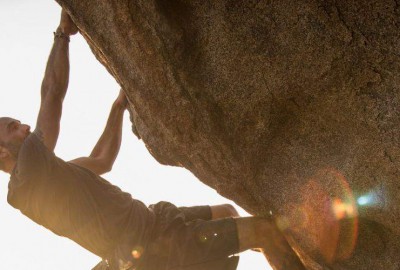 Un hombre escalando una roca con el sol detrás de él.