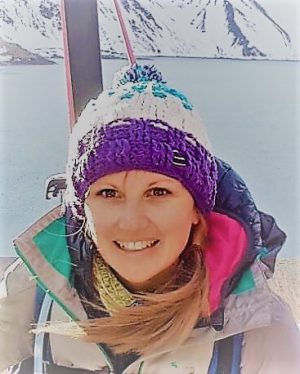 Una mujer con un sombrero morado sonriendo frente a una montaña nevada.