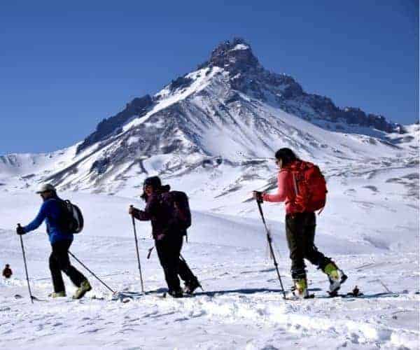 Un grupo de esquiadores caminando en la nieve con una montaña al fondo.