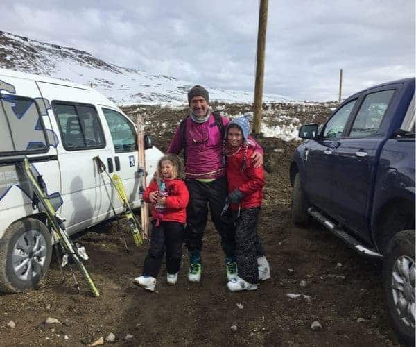 Un hombre y dos niños parados junto a una furgoneta en una montaña nevada.