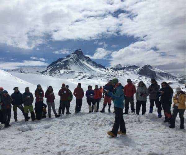 Descripción: Un grupo de personas de pie frente a una montaña cubierta de nieve.