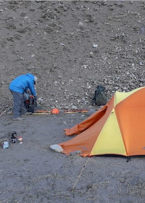 Un hombre está instalando una tienda de campaña en la ladera de las montañas de los Andes.