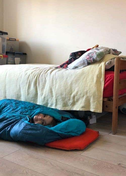 Un niño de familia durmiendo en un saco de dormir en el suelo.