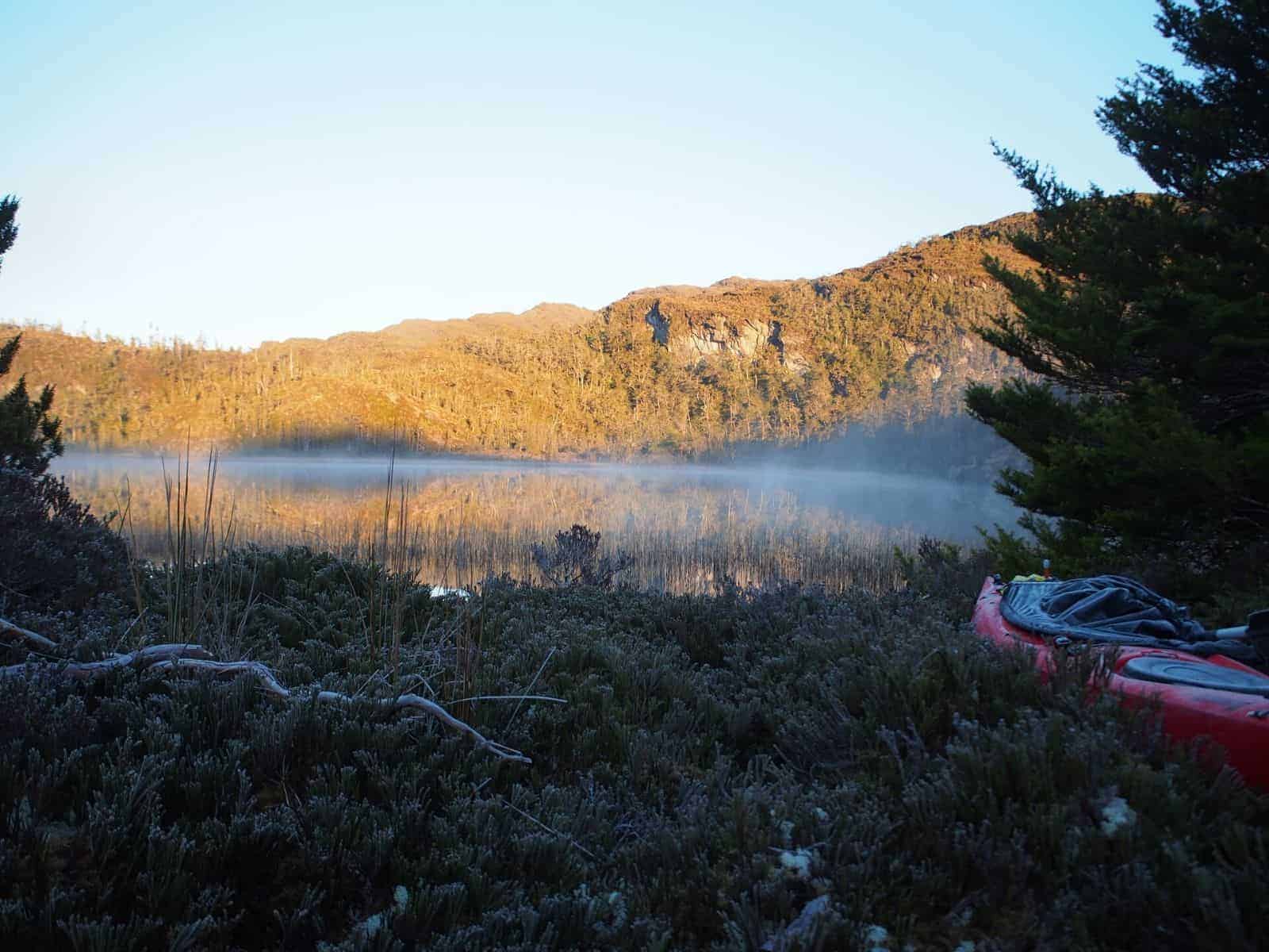 Un kayak rojo se encuentra en la hierba junto a un lago.