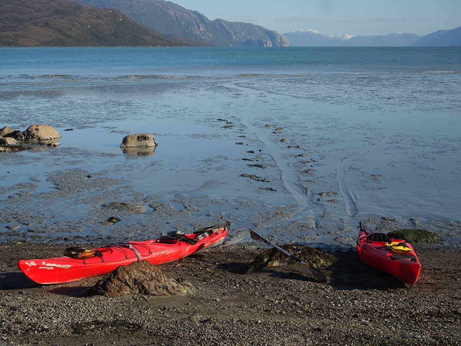 Dos kayaks rojos en la orilla de un cuerpo de agua cerca de una tienda de alquiler de kayaks.