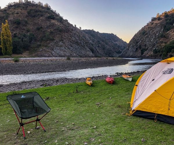 Una tienda de campaña se encuentra sobre el césped junto a un río, perfecta para acampar.