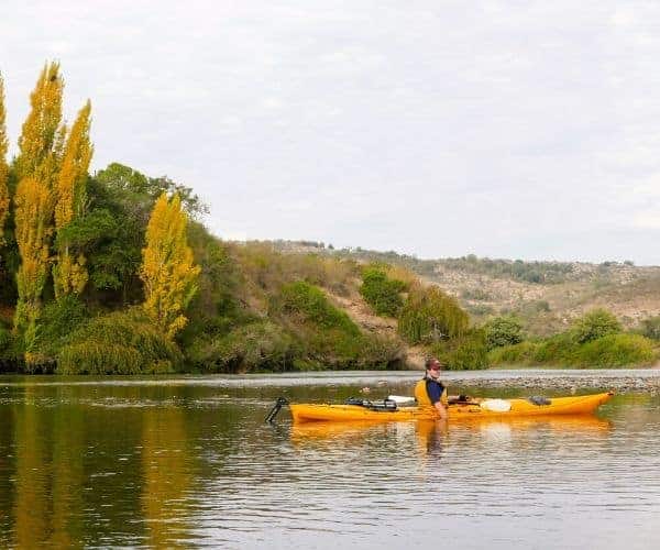 Una persona rema en un kayak en un río cerca de los árboles mientras acampa.