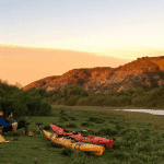 Dos kayaks y una tienda de campaña montada para acampar junto a un río.