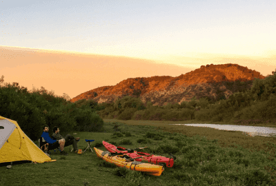 Dos kayaks y una tienda de campaña montada para acampar junto a un río.