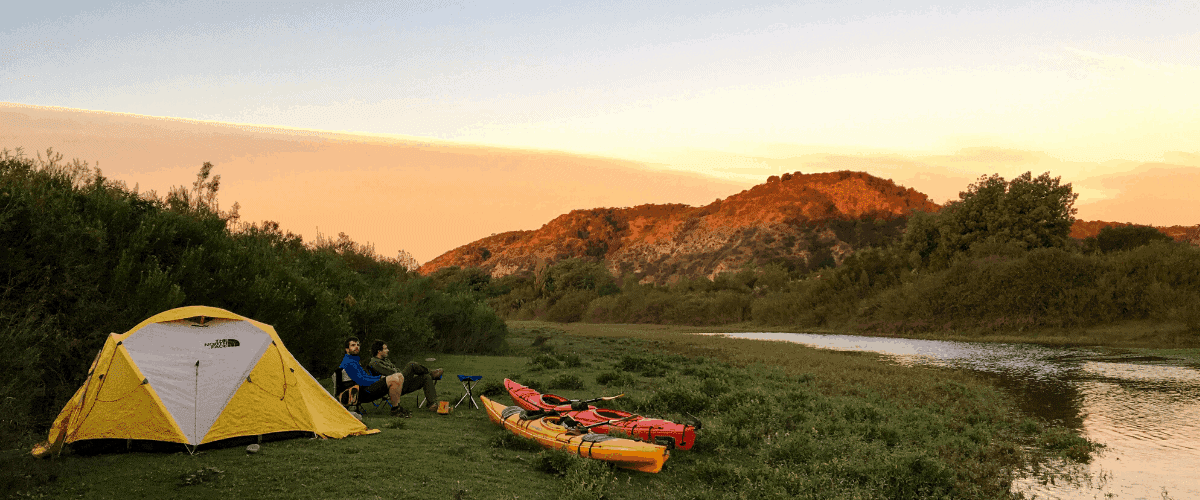 Dos kayaks y una tienda de campaña montada para acampar junto a un río.