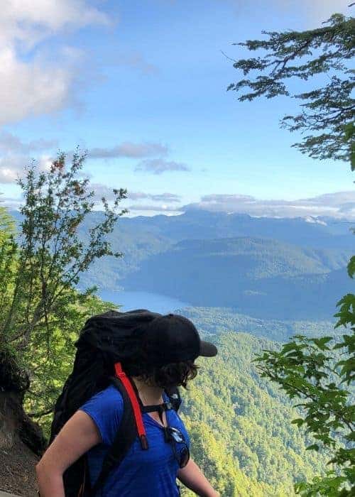 Una mujer caminando por un sendero con montañas al fondo.