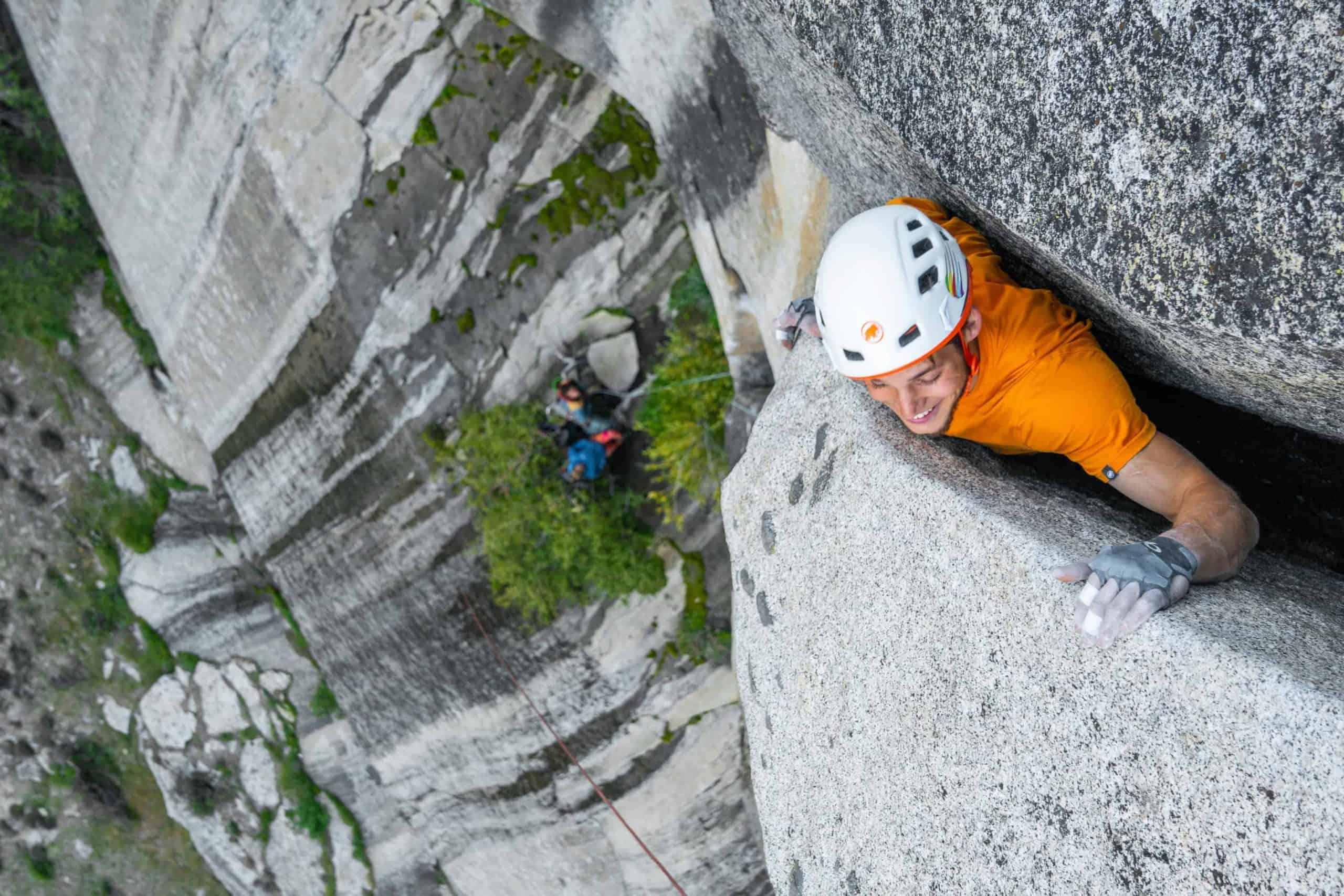 Un hombre con una camisa naranja trepa a una roca en Yosemite.
