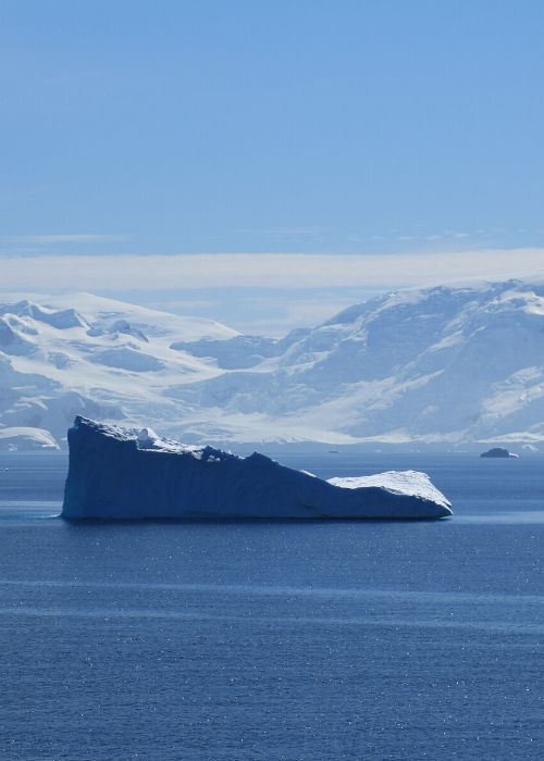 Un iceberg extremo flotando en el agua cerca de las montañas.