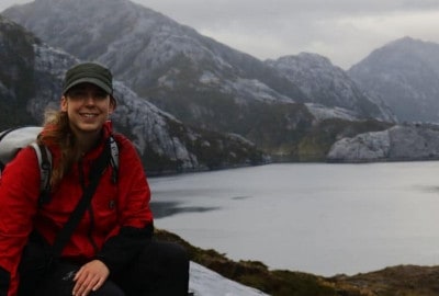 Una mujer, Paula López, sentada en lo alto de una montaña extrema junto a un lago.