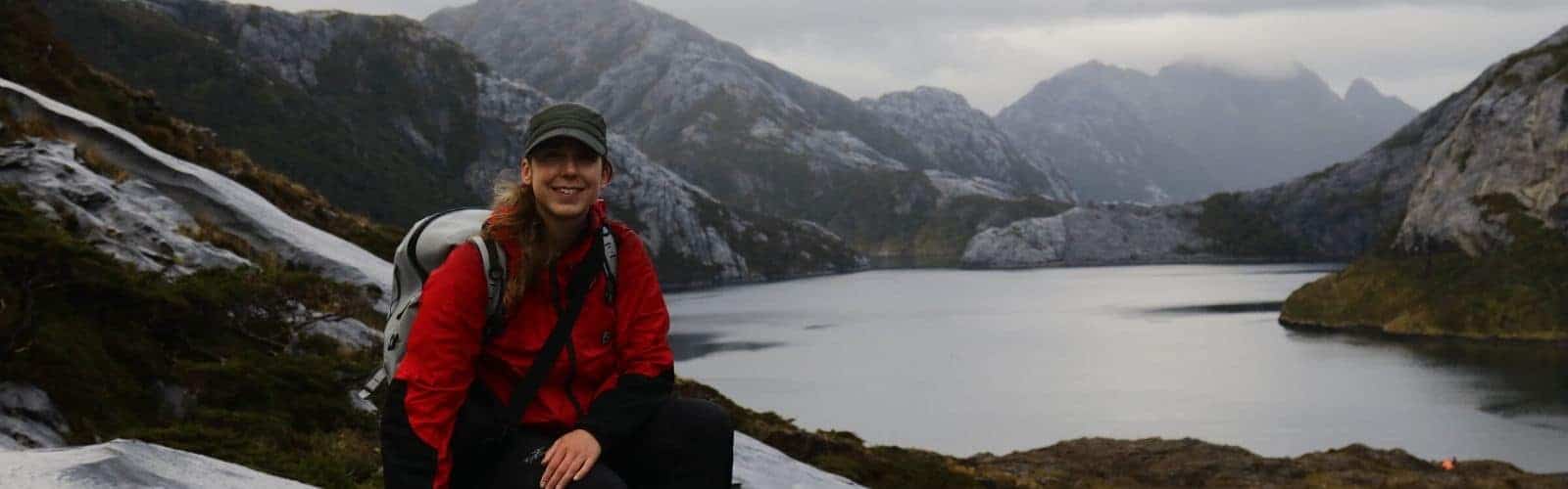 Una mujer, Paula López, sentada en lo alto de una montaña extrema junto a un lago.